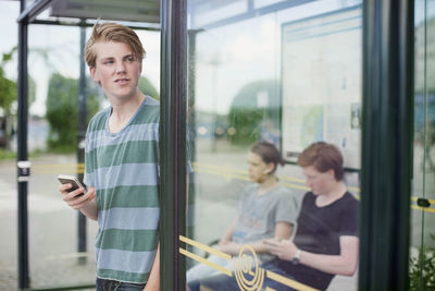 Young man looking through camera while standing on window
