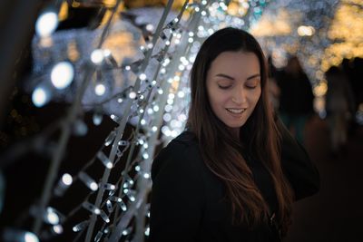 Close-up of smiling woman looking down by illuminated string lights