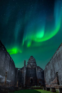 Low angle view of built structure against aurora borealis at night