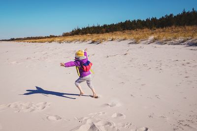 Full length of girl running on sand at beach against clear sky