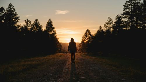 Rear view of silhouette woman walking on street against sky during sunset