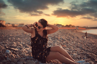 Midsection of woman at beach against sky during sunset