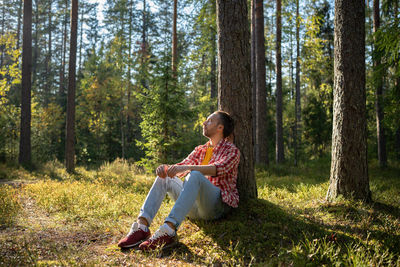 Man resting sitting near tree in forest with closed eyes in warm sunny day.