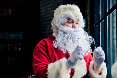 Man wearing santa claus costume standing by window at home