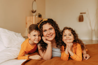 A happy mother hugs her children a little boy and a girl in pajamas sitting on bed in cozy interior 