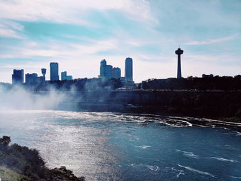 River and waterfall by buildings in city against sky in niagara