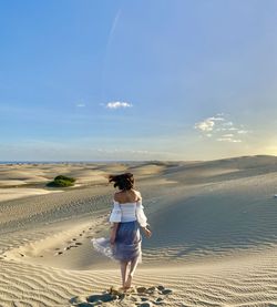 Rear view of woman walking on beach against sky