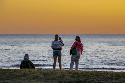 Rear view of people on beach against sky during sunset