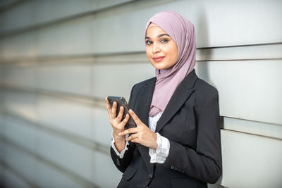 Portrait of businesswoman holding mobile phone while standing against shutter
