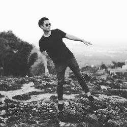 Young man balancing on rock against sky