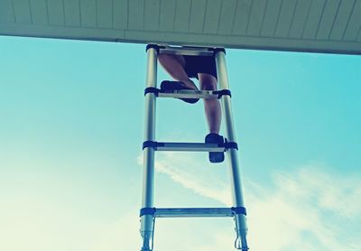 Low angle view of man on ladder against blue sky