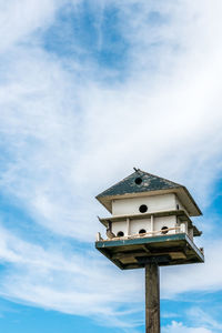 Low angle view of birdhouse on against sky - big 2 storey birdhouse with nests and a solo bird. 