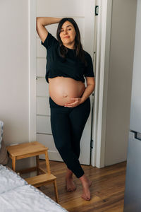 Brunette pregnant woman hugging her tummy while standing at home