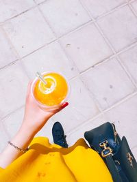 High angle view of woman holding yellow glass on tiled floor