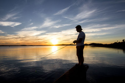 Silhouette man fishing at lake against sky during sunset