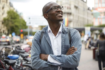 Smiling mid adult businessman looking up while standing with arms crossed in city