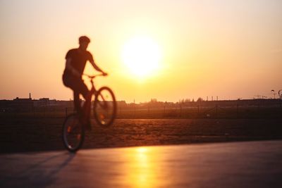 Silhouette man riding bicycle on street against sky during sunset