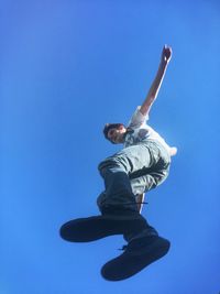 Low angle view of woman jumping against clear sky