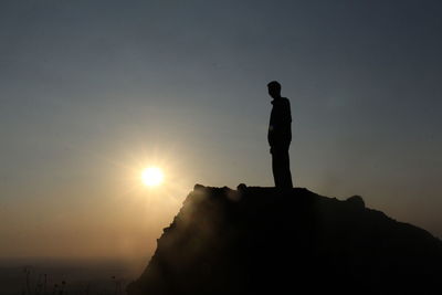 Silhouette man standing on rock against sky during sunset