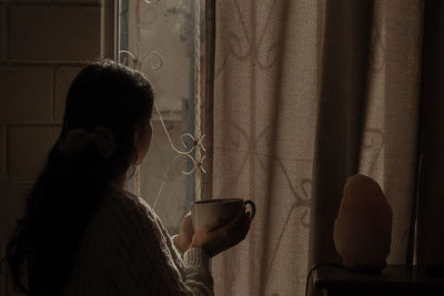 Rear view of woman standing by window at home