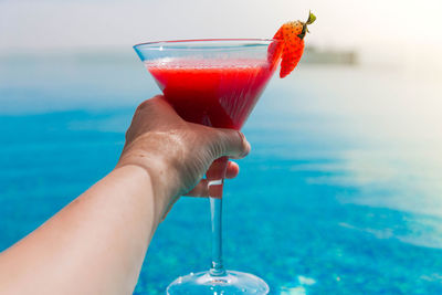 Cropped image of hand holding drink against sea