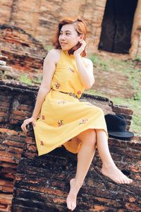 Smiling young woman looking away while sitting against built structure