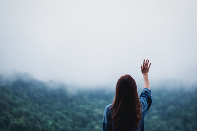 A female traveler raising hand and looking at a beautiful green mountain on foggy day