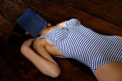 Woman in bodysuit with book lying down on hardwood floor
