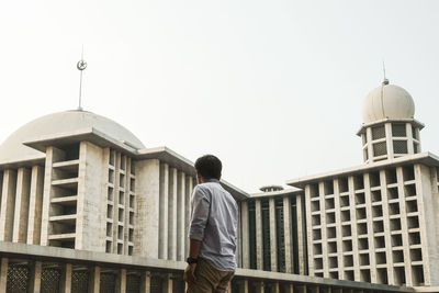 Rear view of man standing by building against clear sky