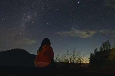 Rear view of man sitting against sky at night