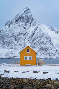 Yellow house by lake against snowcapped mountain