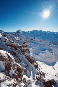 Scenic view of snowcapped mountains against blue sky on sunny day