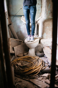Low section of woman standing on toilet bowl at abandoned room