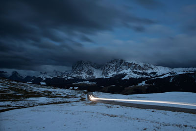 Light trails on road amidst snow covered landscape at dusk