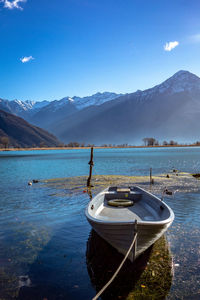 Sailboats moored on lake by mountains against blue sky