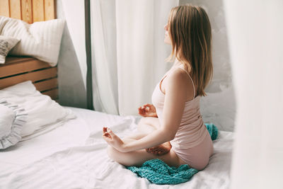 A young woman in pyjamas is sitting on a bed in a lotus position 