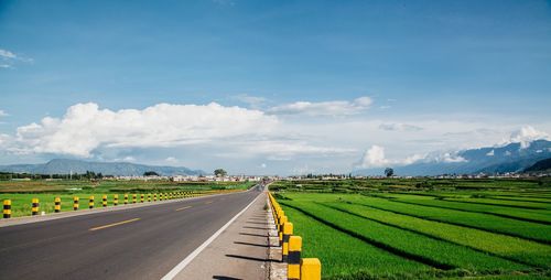 Country road amidst fields against cloudy sky