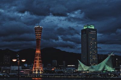 Illuminated buildings in city against cloudy sky