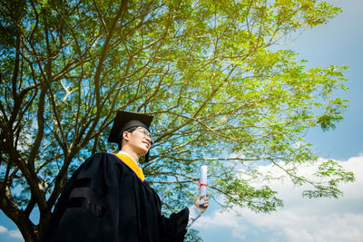 Young man in graduation gown standing against sky