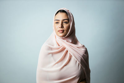 Young woman wearing hijab standing against gray background