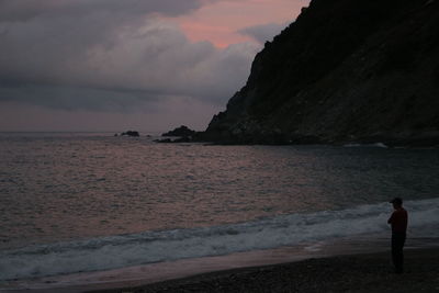 People standing on beach against sky during sunset