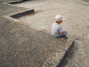 High angle view of boy looking away sitting on footpath 