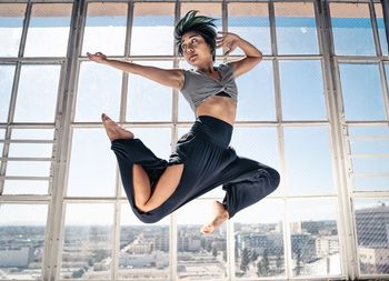 Full length of woman jumping in city against sky