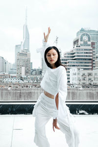 Portrait of young woman against white buildings in city