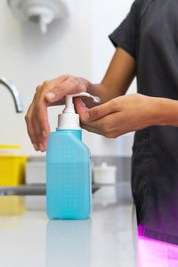 Faceless female doctor in uniform disinfecting hands with antibacterial gel in plastic bottle placed on table in medical room