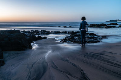 Rear view full length of woman standing at beach during sunset