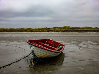 Boat moored on beach against sky