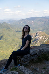 Portrait of young woman sitting on rock against mountain