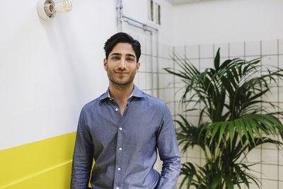 Portrait of confident young man standing by wall in creative office