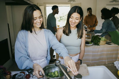 Happy female friends preparing dinner together in kitchen at home